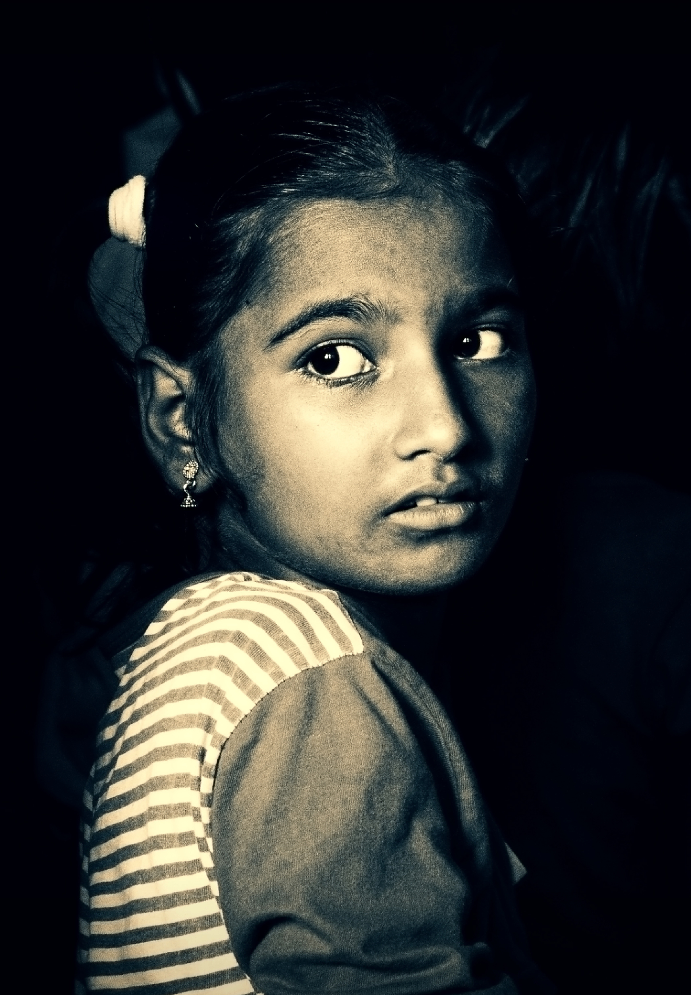 A young girl turned away, looking back towards the camera in low light