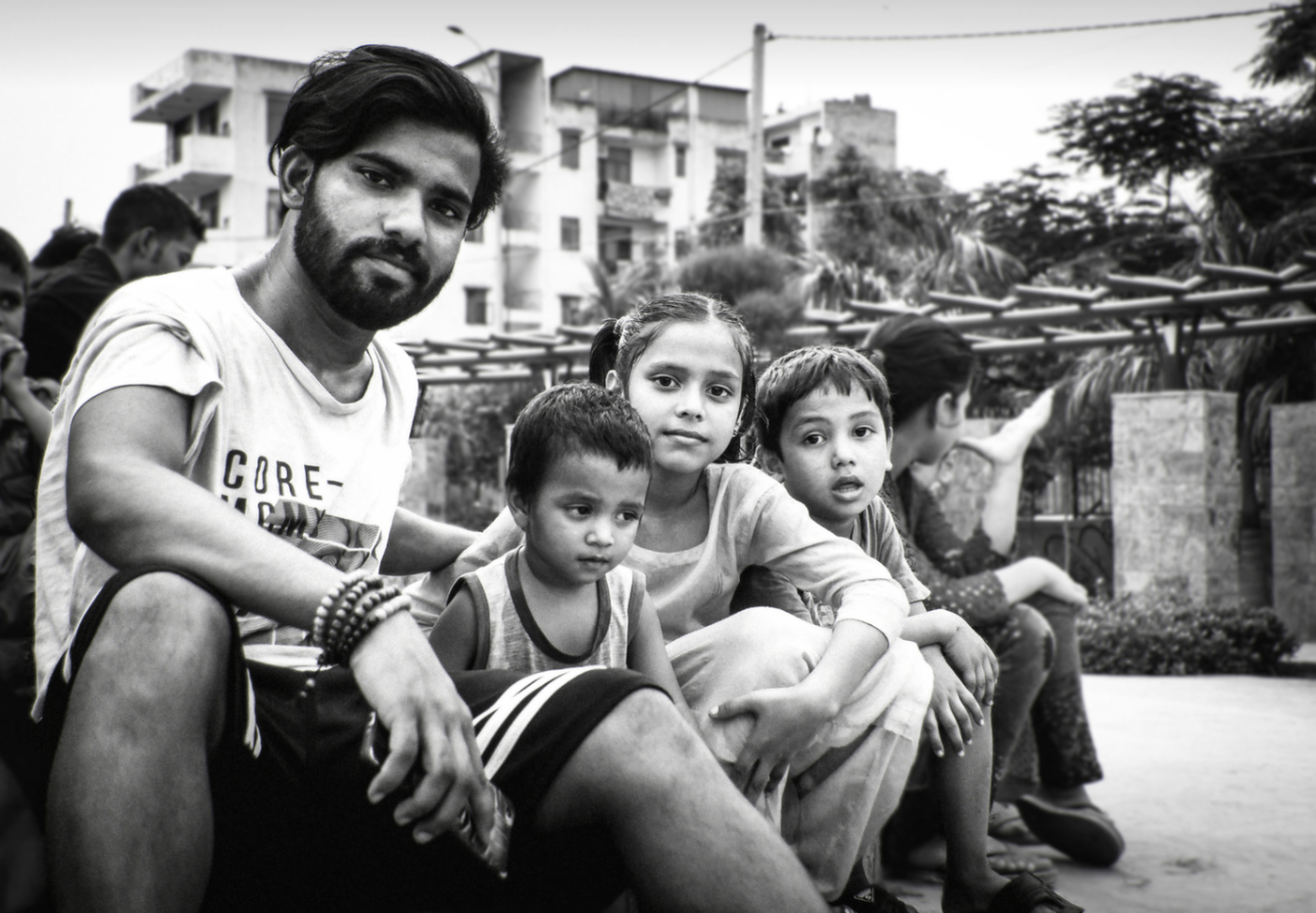 A young man sitting among a group of children in a residential neighbourhood, black and white