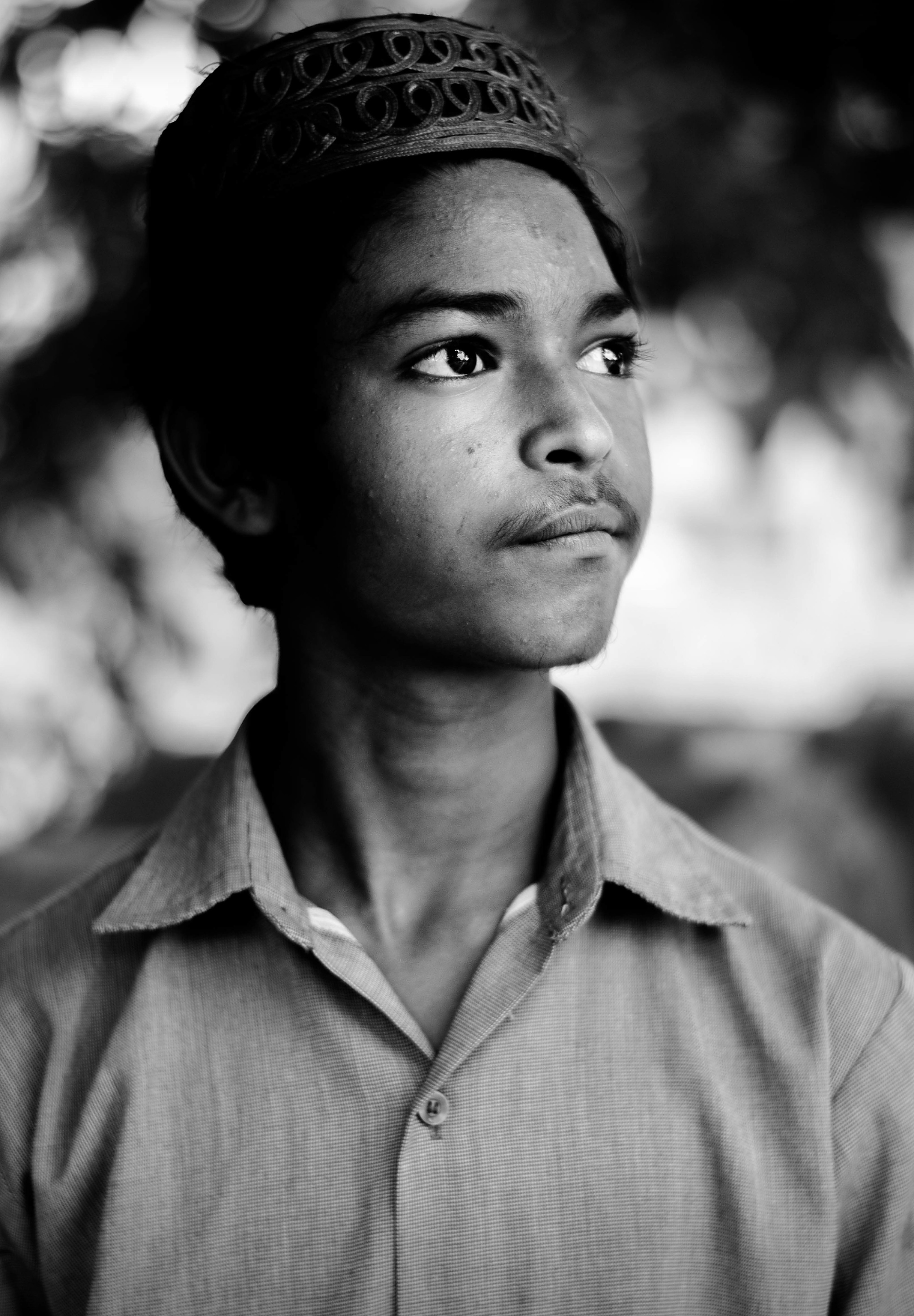 Close black and white portrait of a boy in a cap looking beyond the camera
